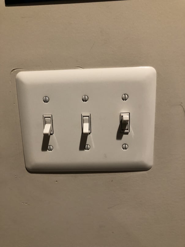 The switch panel in my bedroom, with three two-way switches. The first two are turned off, while the third, which controls the light, is turned on.